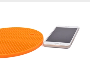 Orange round honeycomb silicone mat with hanging hole next to a smartphone for size