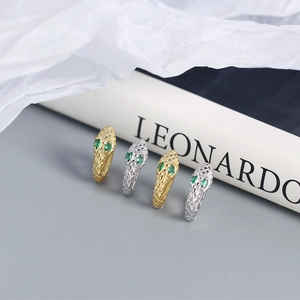 Detail of snake-shaped silver earrings in gold and silver with green gemstone eyes