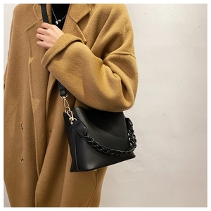 Detail of black bucket bag featuring a woven top handle and gold-tone metal hardware