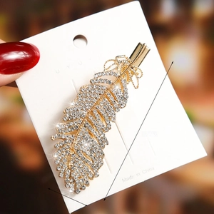 Macro shot of 6.5cm gold-plated feather hair clip with rhinestones on white card