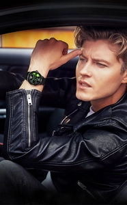 Men's black racing wheel watch with green accents worn in a luxury car interior