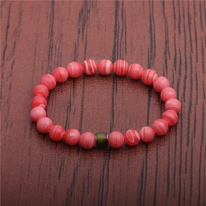 Close-up of pink striped beads and green cylinder accent on a wooden surface
