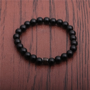 Detail view of black obsidian bead bracelet with a central bronze metal cylinder charm