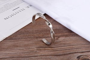 Detailed close-up of a silver twisted open C-shaped cuff bracelet on a white book cover