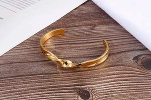 Detailed close-up of a twisted golden cuff bracelet on a dark wooden textured surface