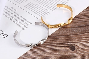 Macro shot of gold and silver twisted cuff bracelets on an open book over wood