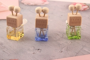 Close-up of square colorful glass car aroma bottles with engraved wooden caps on grey surface