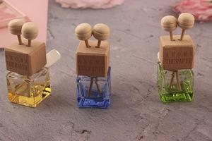 Three colorful square glass car perfume bottles with wooden caps on a textured surface