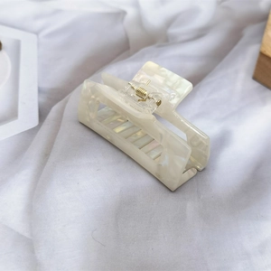 Detail of cream white acetate hair claw clip with shell texture and golden metal spring