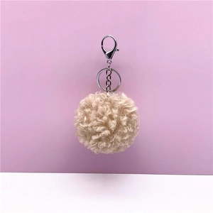 Detail of curly cream fur pom-pom keychain with silver lobster clasp on pink background