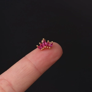 Macro shot of tiny gold crown earring with pink marquise zirconias held on fingertip