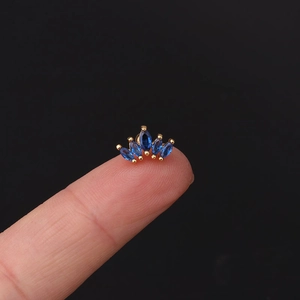 Macro shot of gold-plated crown ear stud with blue marquise zircon on a fingertip