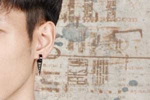Vue détaillée d'une boucle d'oreille triangulaire noire mate en acier sur un lobe d'homme