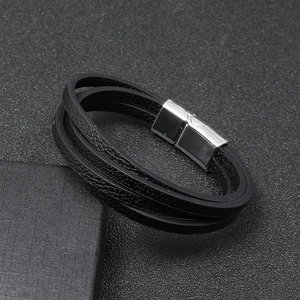 Detalle de una pulsera multicapa de cuero negro con cierre magnético plateado en fondo oscuro