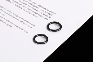 Detailed view of black stainless steel clip-on hoop earrings on white textured paper
