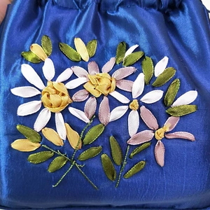 Detailed view of floral ribbon embroidery on a royal blue satin drawstring pouch bag