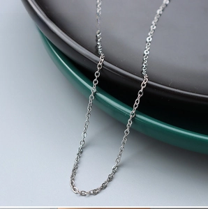 Detail of 1.7mm wide steel cross chain necklace draped over elegant ceramic plates