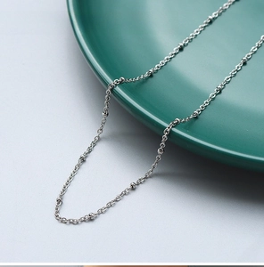 Detailed macro view of a 1.7mm steel cross bead chain on a dark green ceramic plate