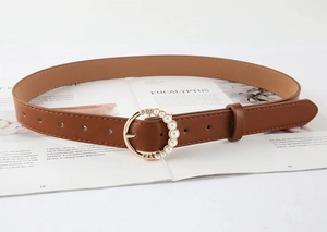 Detail of a brown leather belt with a pearl-decorated round buckle on a magazine background