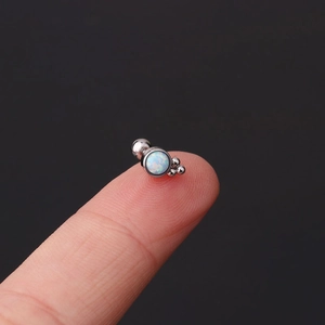 Macro detail of a mini stainless steel cartilage stud with opal stone on a fingertip
