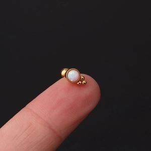 Macro shot of gold opal cartilage stud earring held on fingertip showing mini size