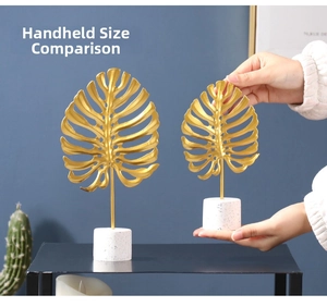 Close-up of golden metal monstera leaf decor with marble base showing size comparison
