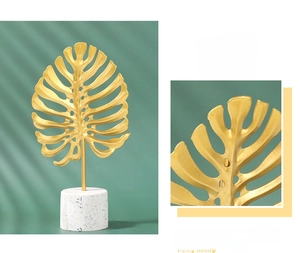 Detail of golden metal monstera leaf ornament with white terrazzo cylindrical base