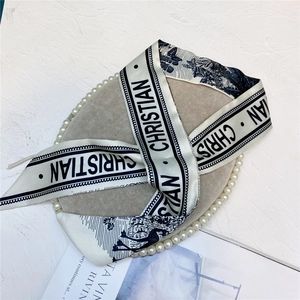 Flat lay of a beige beret with a black and white printed silk scarf and pearl necklace