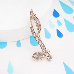 Detailed close-up of a gold musical note brooch with sparkling rhinestones and a pendant
