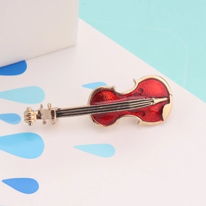 Detailed close-up of a red violin brooch with gold accents and fine musical strings