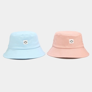 Detailed view of light blue and pink bucket hats with stitched smile patches