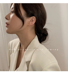Close-up of minimalist gold bar and butterfly stud earrings on a model ear lobe