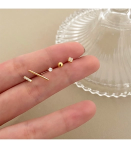 Macro detail of 5-piece gold stud earring set with zircons held on a finger