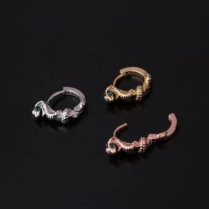 Macro shot of three snake-shaped ear cuffs in gold, silver, and rose gold with green stone eyes