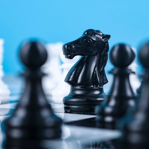 Macro shot of a black knight chess piece made of resin on a board with blue background
