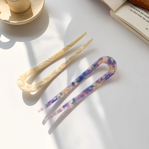 Set of two U-shaped acetate hair pins in marble cream and multicolor patterns on white desk