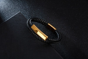 Close-up of black braided leather men's bracelet with gold textured metal plate