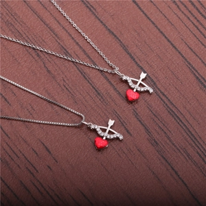 Silver cupid's arrow through a red heart necklace with sparkling zircon on wood background