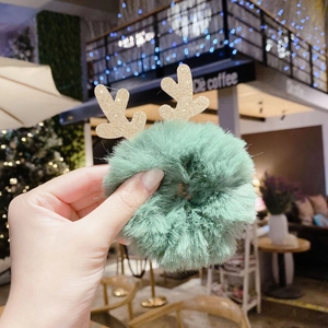 Close-up of a festive green plush hair clip with glittery gold reindeer antlers