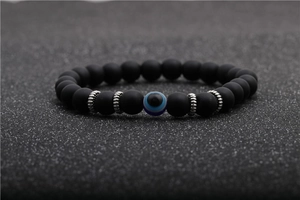 Macro detail of 8mm matte black agate beads with blue evil eye charm on beaded bracelet