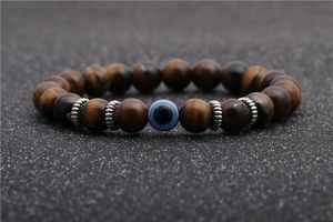 Macro detail of 8mm brown tiger eye beads and evil eye charm on elastic bracelet