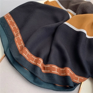 Close-up of soft cotton linen scarf featuring orange contrast border and H letter detail