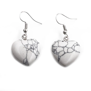 Macro shot of white heart-shaped earrings with black vein texture and metal hooks