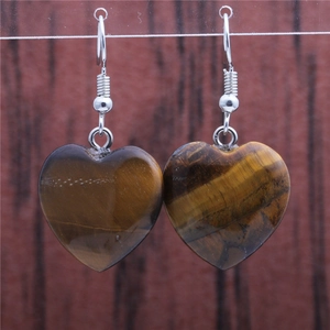 Detailed view of heart-shaped tiger eye stone earrings with silver hooks on wood background