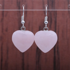 Macro shot of pink heart-shaped crystal pendant earrings with silver hooks on wood