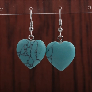 Macro shot of heart-shaped turquoise earrings with silver hooks on a wooden background