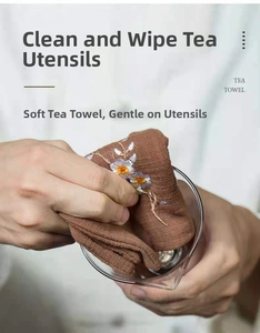 Macro view of hands using a floral embroidered brown linen tea towel to clean glass teaware