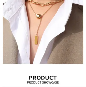 Close-up of double-layered gold necklace with square pendant and tassel over white shirt