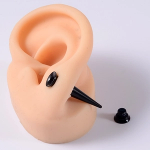Detail view of black acrylic ear taper and plug set on flesh-toned ear model