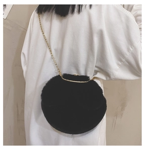 Detail of round black faux fur crossbody bag with thin gold chain strap on model